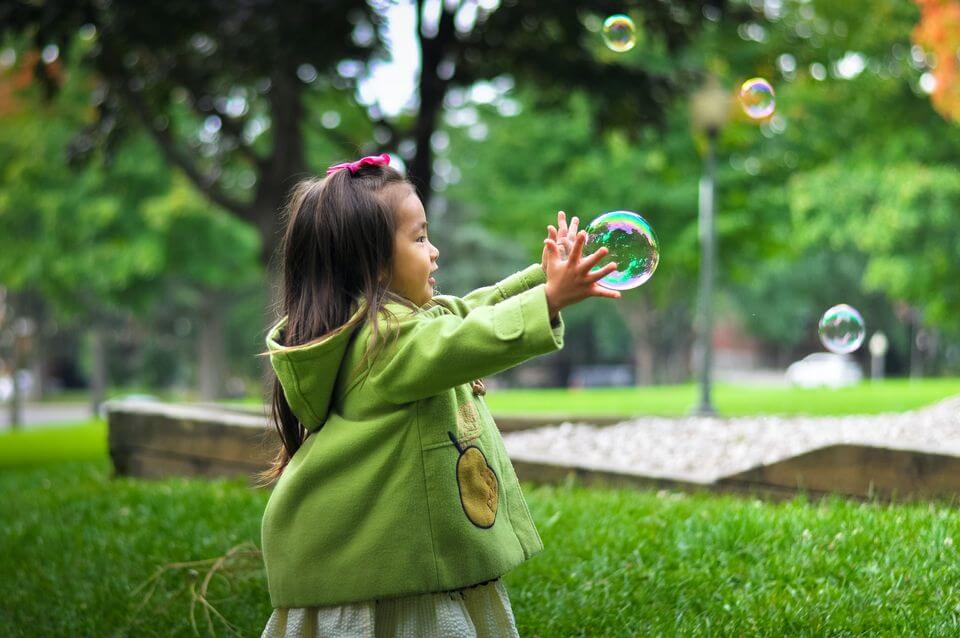 Little girl chasing a foam bubble in the park